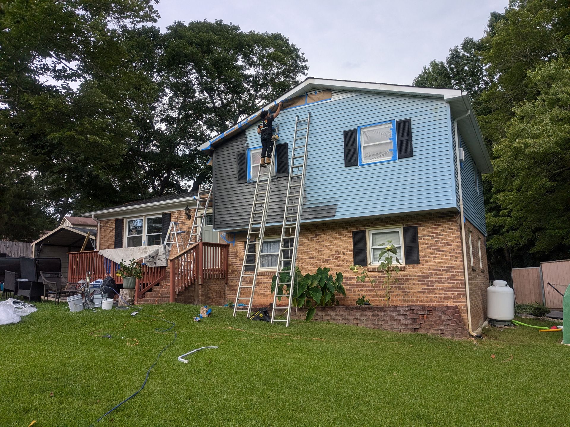 A man on a ladder is painting the side of a house.