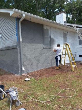 A man is standing on a ladder painting the side of a house.