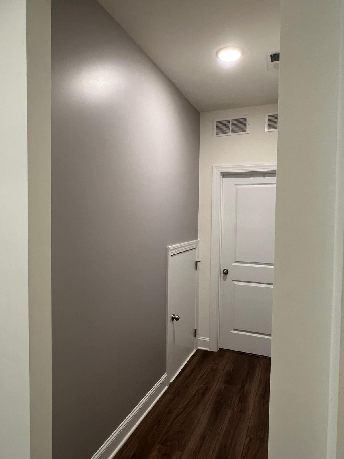 A hallway with a white door and a gray wall.