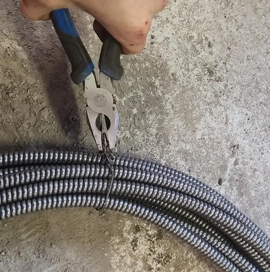 Une personne tient une paire de pinces au-dessus d'un tuyau.