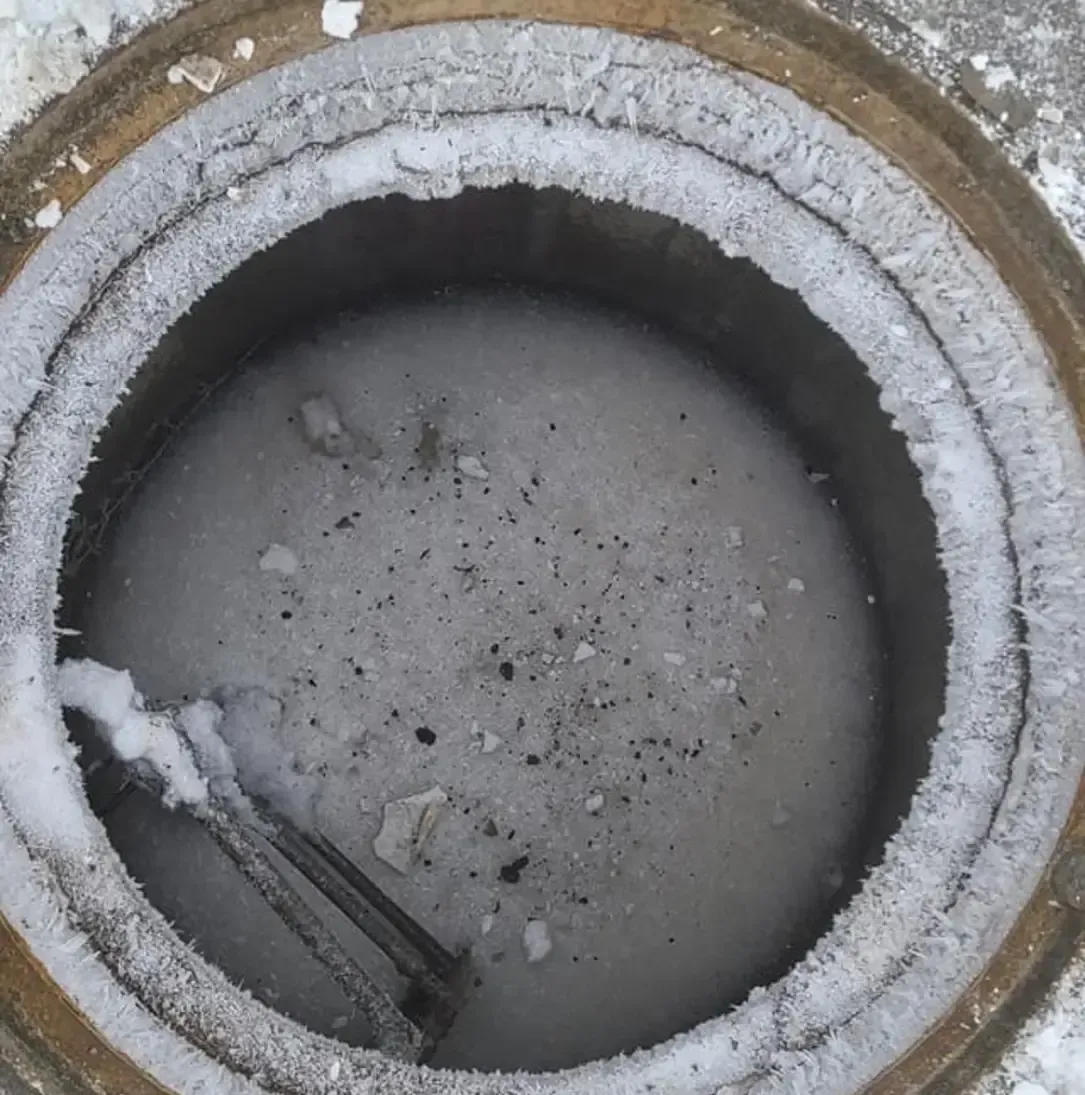 Un couvercle de trou d'homme est recouvert de neige et de glace