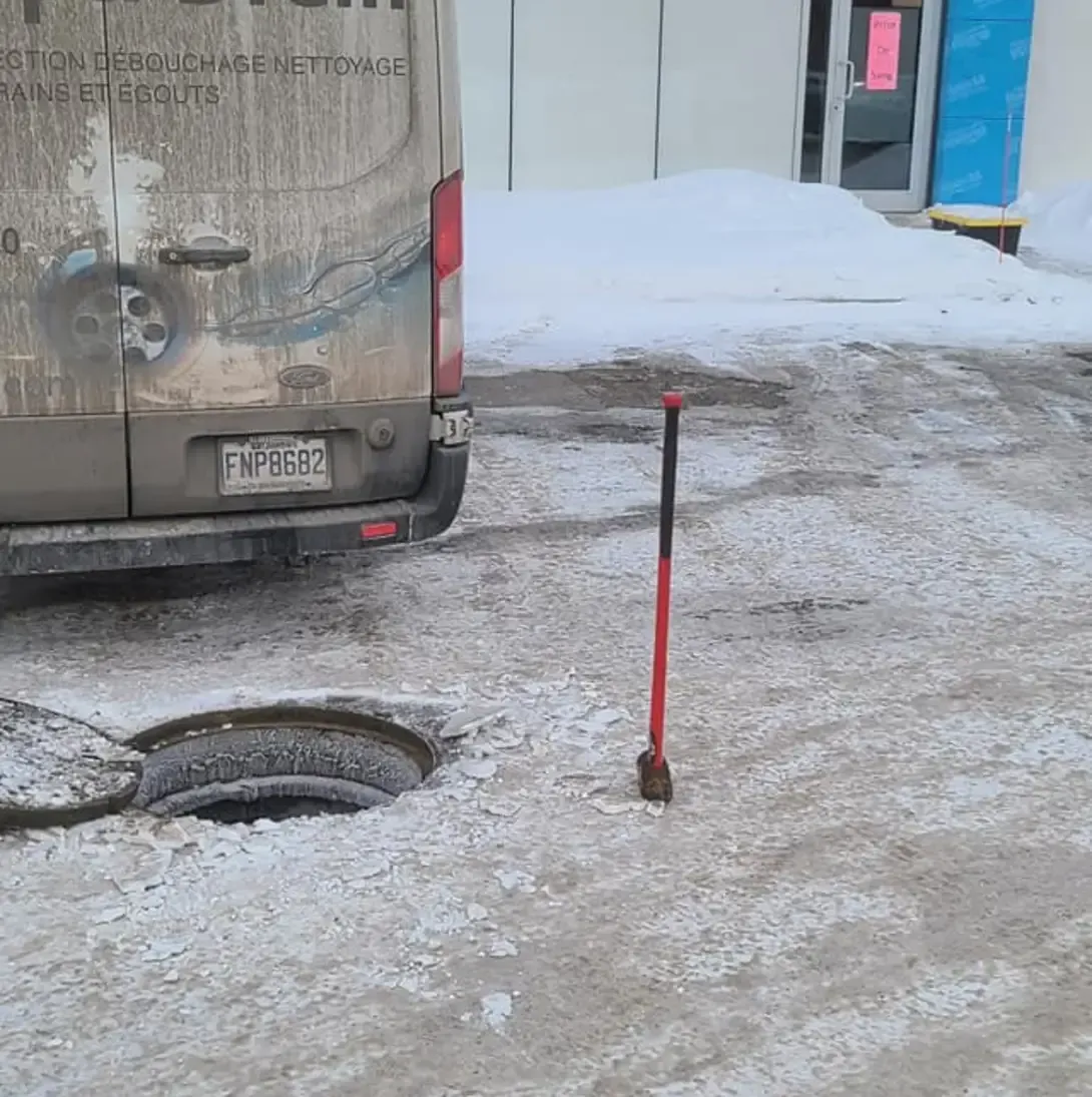 Une camionnette est garée à côté d'une plaque d'égout dans la neige.