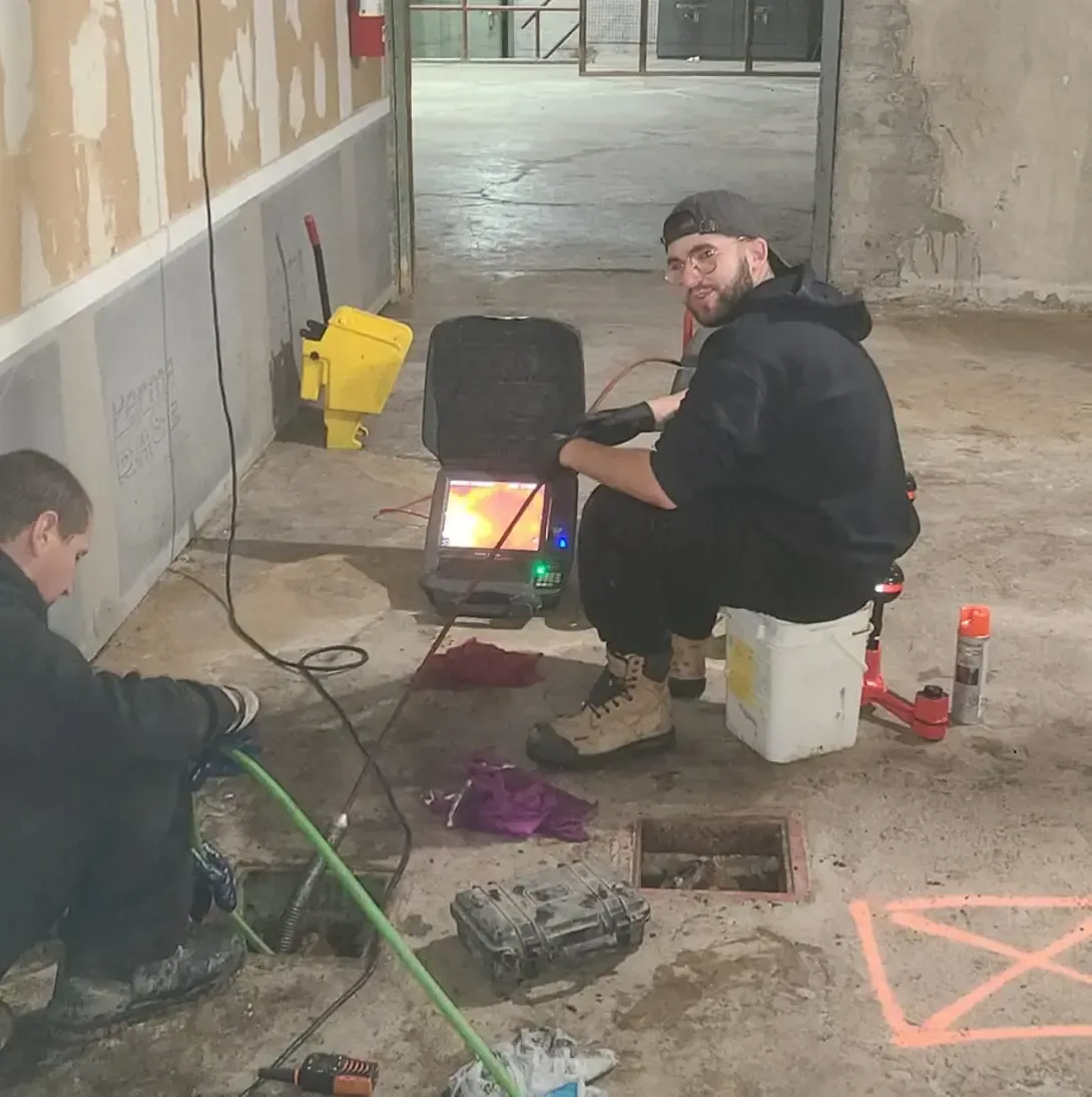 Deux hommes travaillent sur un drain dans un bâtiment.