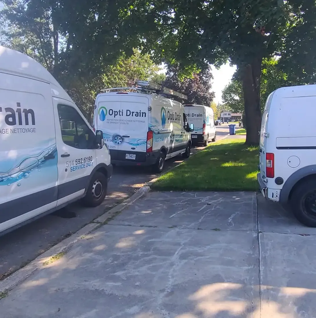 Plusieurs camionnettes sont garées sur le bord de la route dont une sur laquelle est écrit opti drain