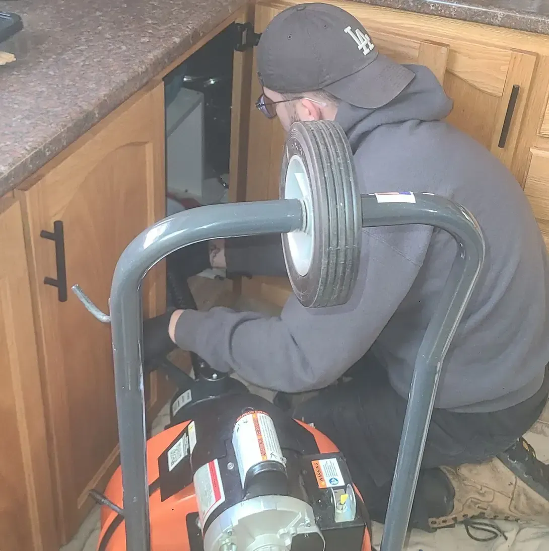 Un homme est à genoux dans une cuisine et utilise un déboucheur.