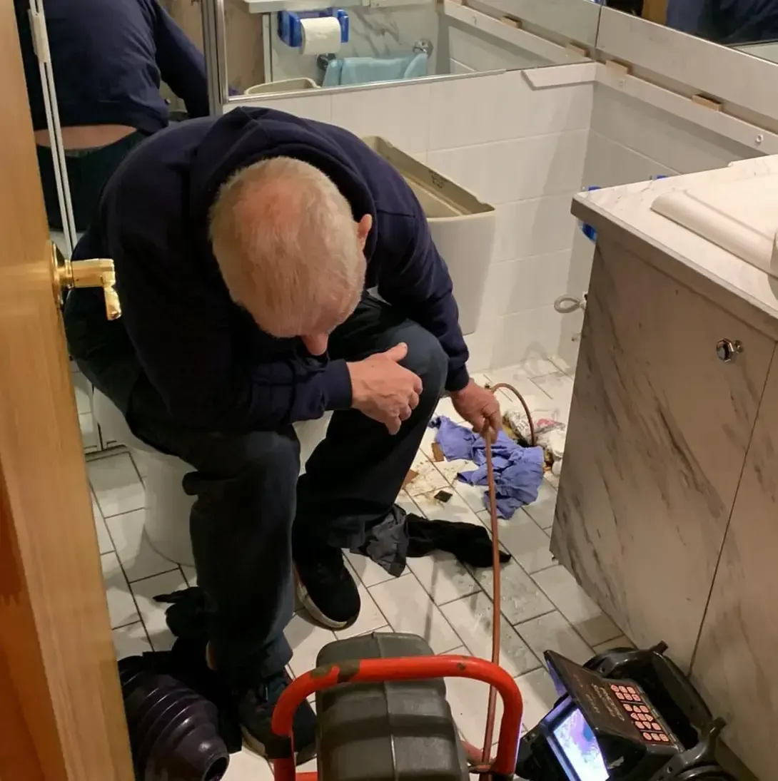 Un homme est à genoux dans une salle de bain et regarde un drain