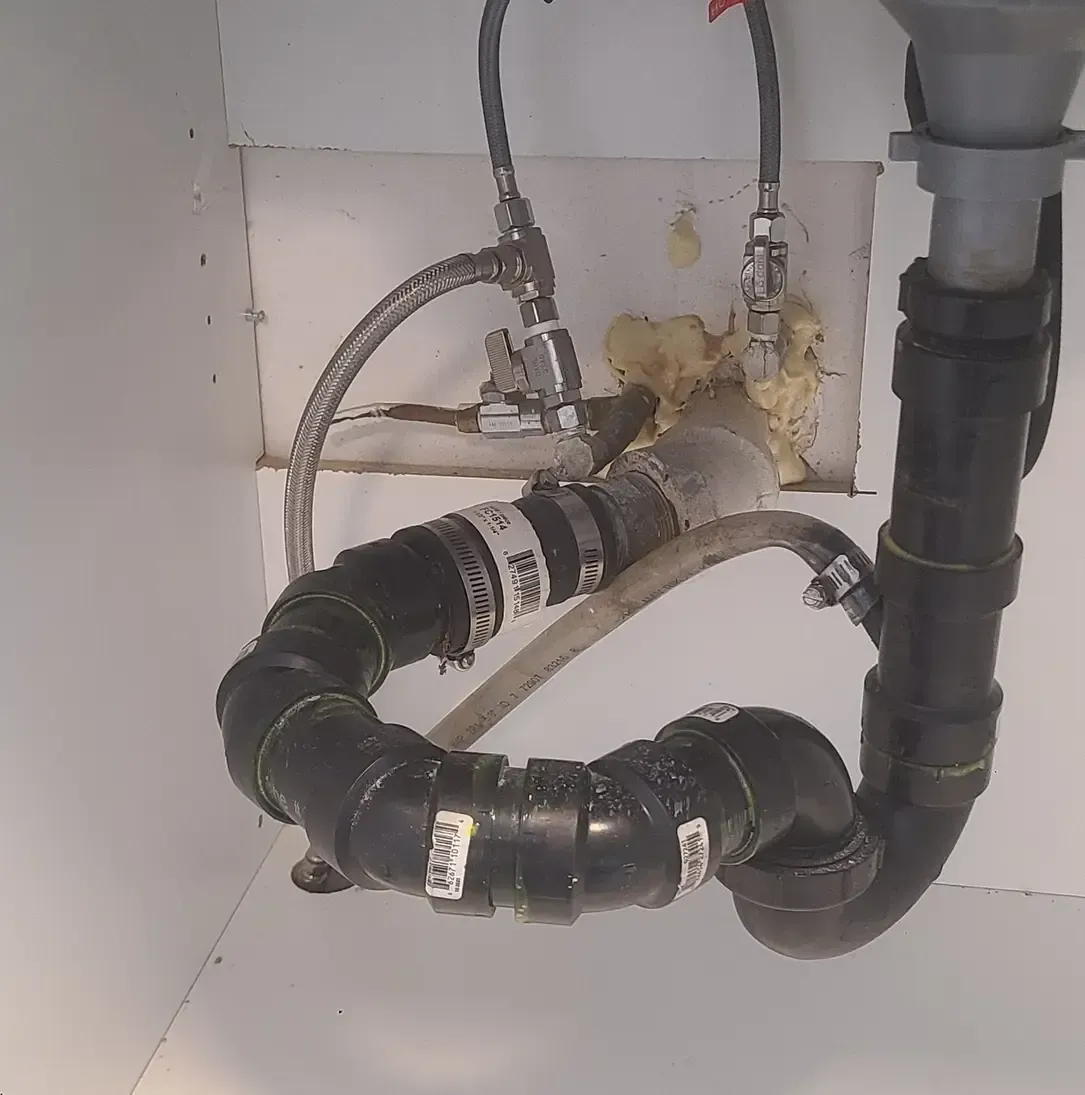 Un tas de tuyaux sous un évier avec un sur lequel est écrit « drain »