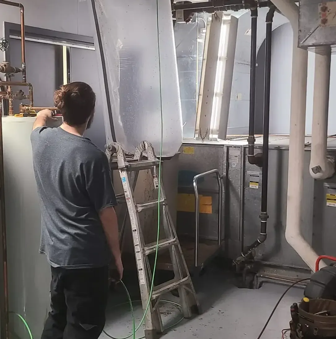 Un homme se tient debout à côté d'une échelle dans une pièce avec des tuyaux.