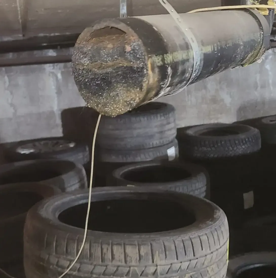 Un gros tuyau est suspendu au-dessus d'un tas de pneus