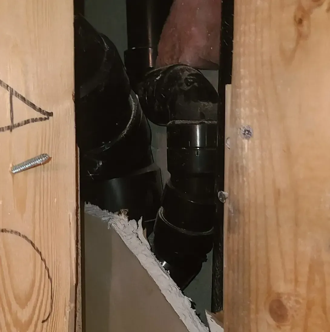 Une personne travaille sur un tuyau dans un mur en bois.