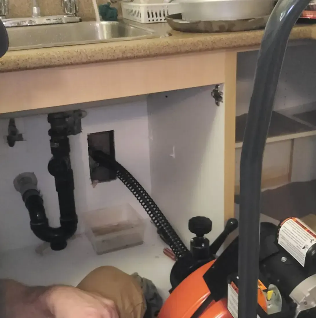 Une personne travaille sous un évier avec un tuyau attaché à celui-ci