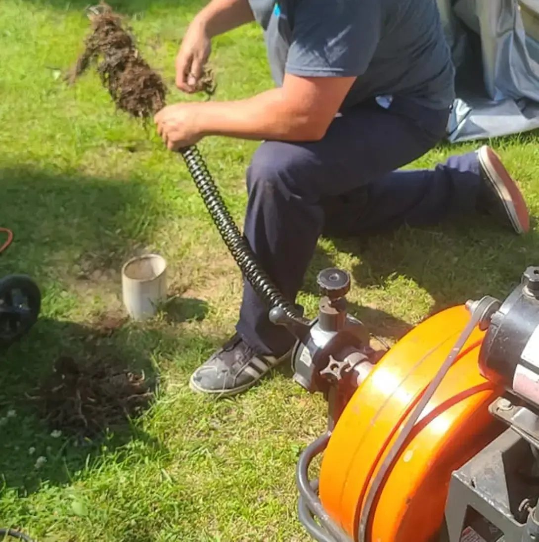 Un homme est agenouillé dans l'herbe et tient un tuyau.