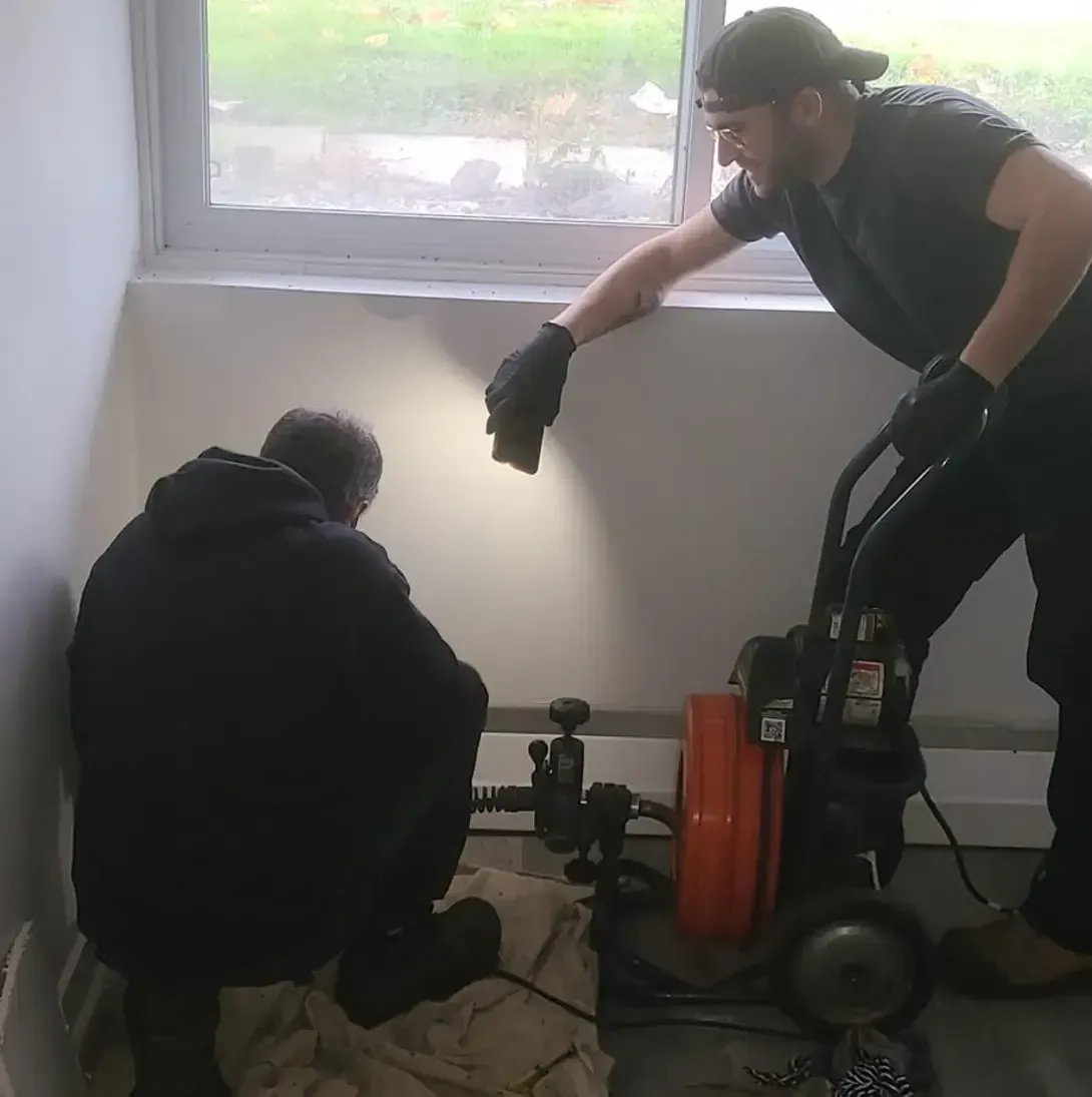 Deux hommes travaillent sur un tuyau dans une pièce.