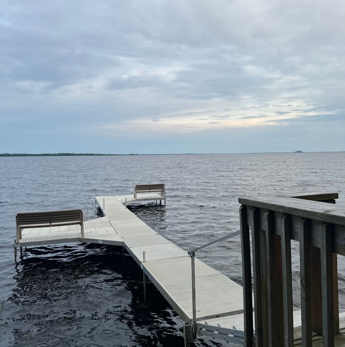 A dock with two benches extends into a dark lake under a cloudy sky.