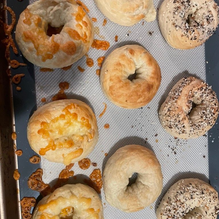 Bagels on a baking sheet; some are cheese-topped, others plain or with seeds.
