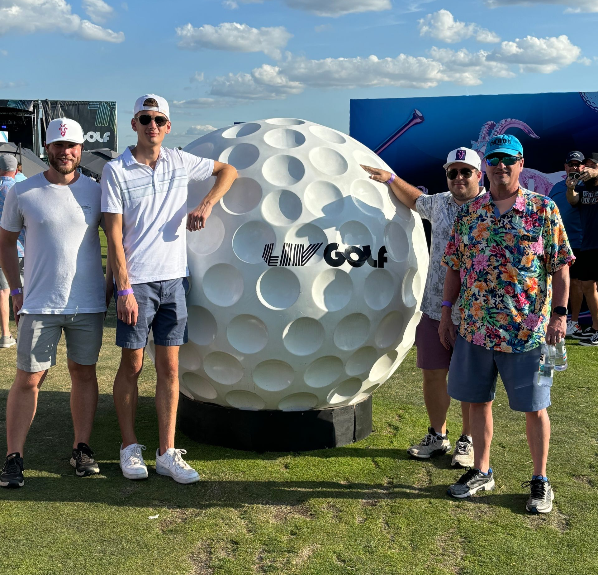 Baseball game at Wrigley Field: Fans in blue hats watch the game on a sunny day. Large scoreboard visible.
