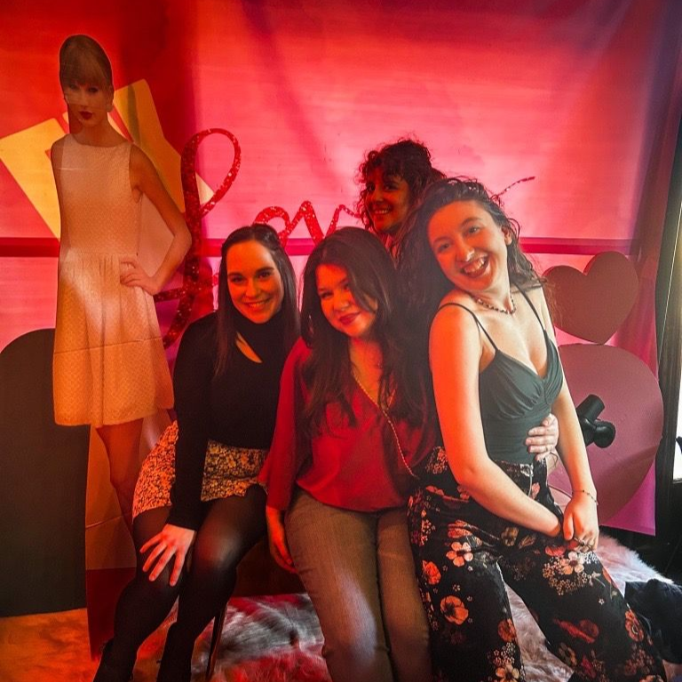 Group of five women pose, smiles, in front of a 