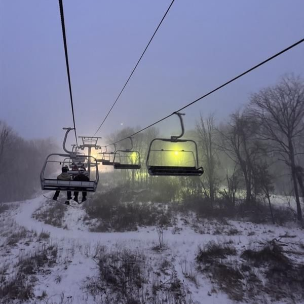 People on ski lift ascending a snowy mountain on a sunny day.