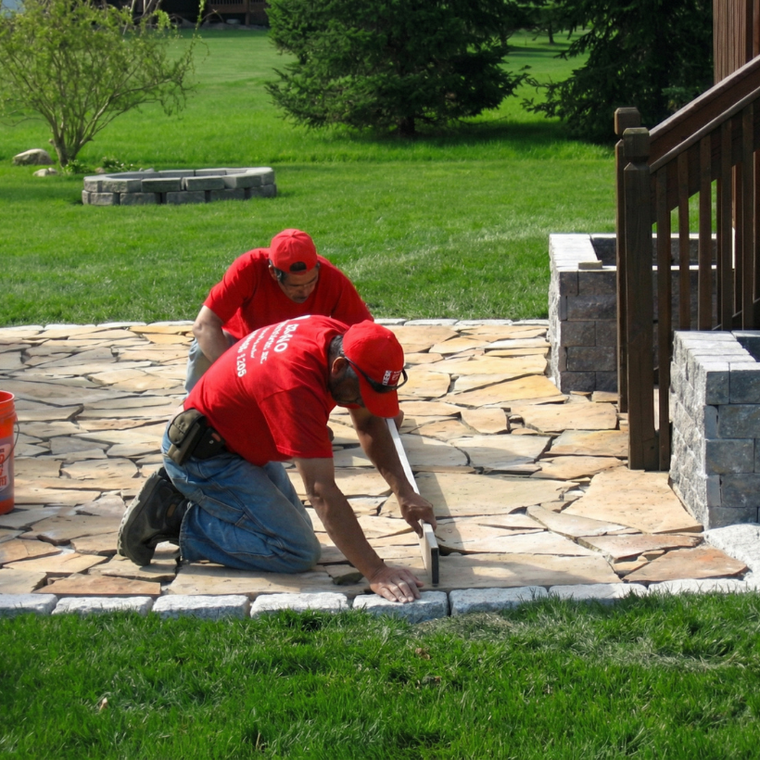 Two workers of Bako Landscaping in red uniforms kneeling on a stone patio