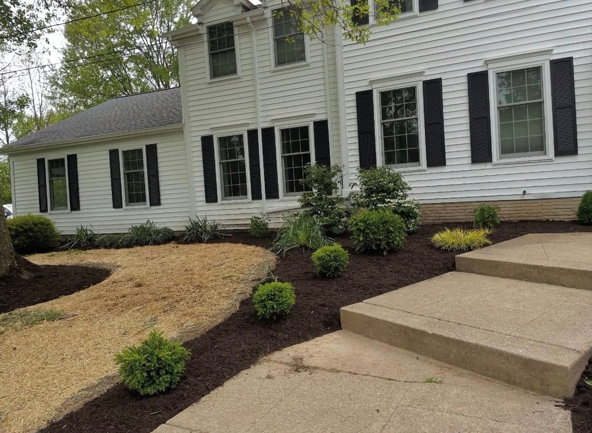 Front view of a white house with black shutters, featuring a landscape with gravel, dark mulch, and small green shrubs.