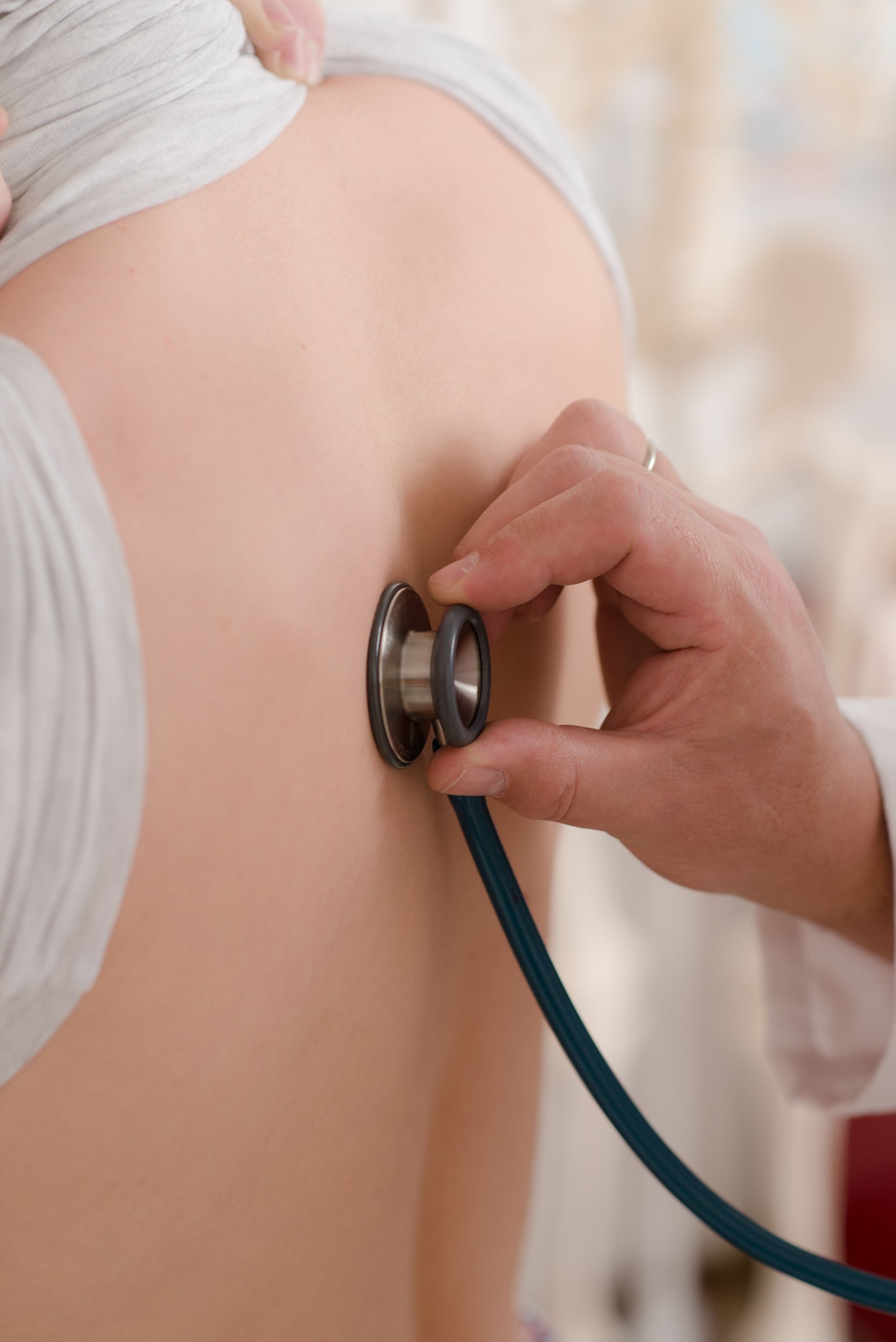 Ein Arzt oder eine medizinische Fachkraft hört während einer Untersuchung den Rücken eines Patienten mit einem Stethoskop ab.