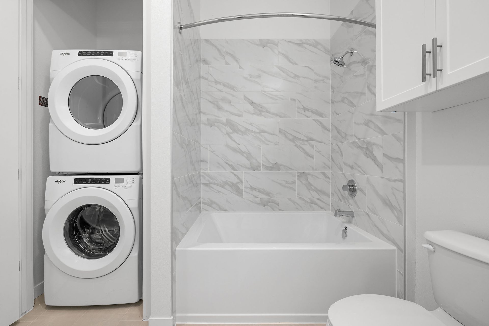 A bathroom with a washer and dryer stacked on top of each other next to shower bath/tub with marble backsplash at The Everett, offering apartments for rent in Northwest Austin, TX