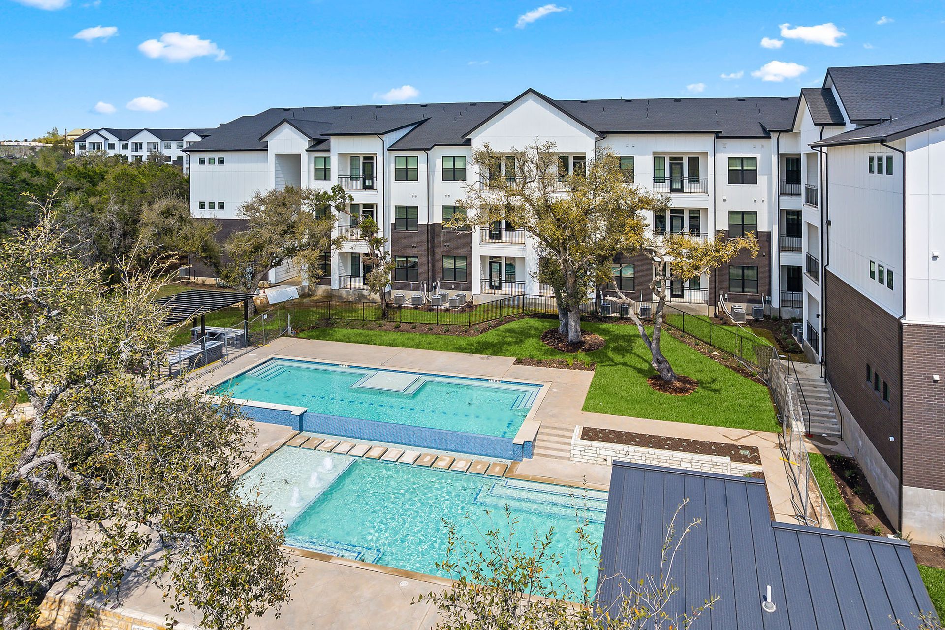An aerial view of a large apartment building with two swimming pools in front of it at The Everett, offering apartments near the Anderson Mill neighborhood.