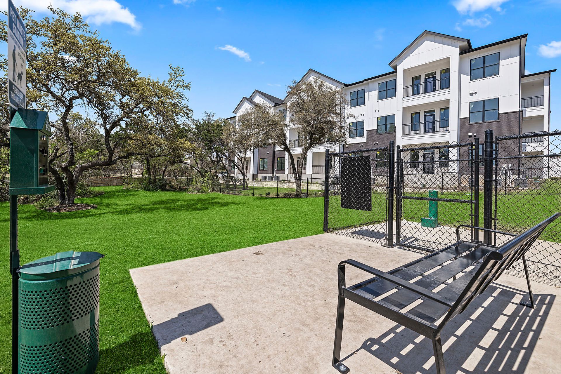 A pet park with a bench and a trash can in front of a building at The Everett, offering apartments for rent near the Plaza Volente neighborhood.