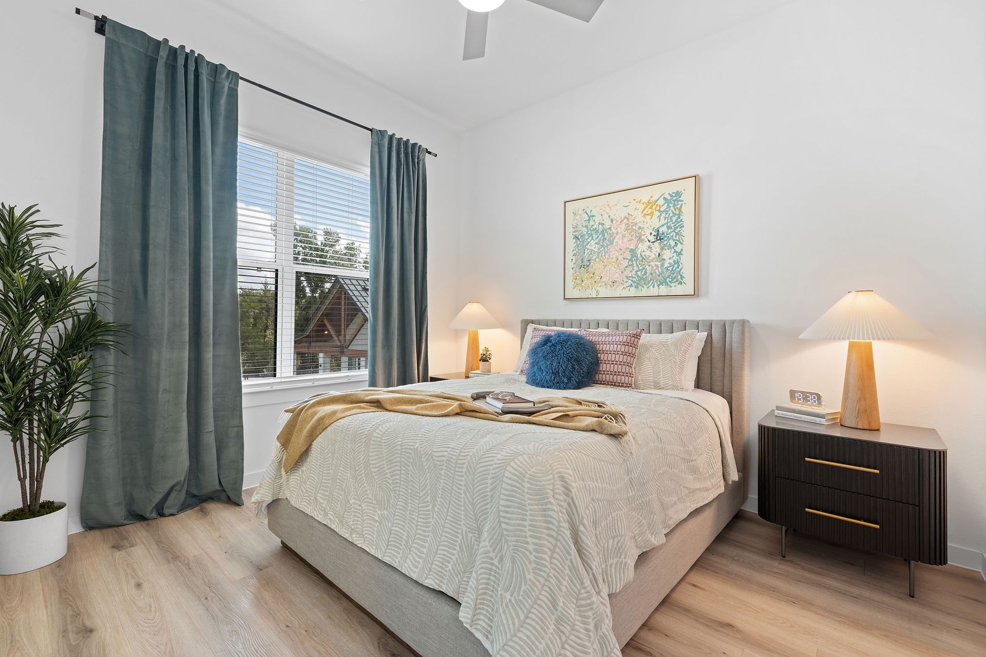 A modern bedroom with a bed , nightstand , lamps and an oversized window at The Everett, offering apartments for rent in Northwest Austin, TX