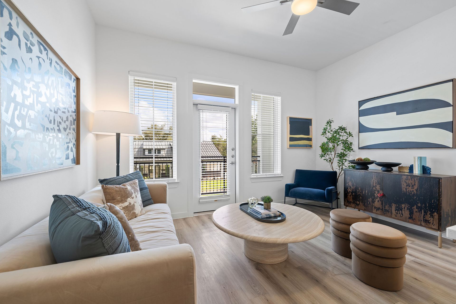 Apartment living room with a couch, table, chairs, a ceiling fan, windows, and door leading to apartment balcony at The Everett, offering apartments for rent in Northwest Austin, TX.
