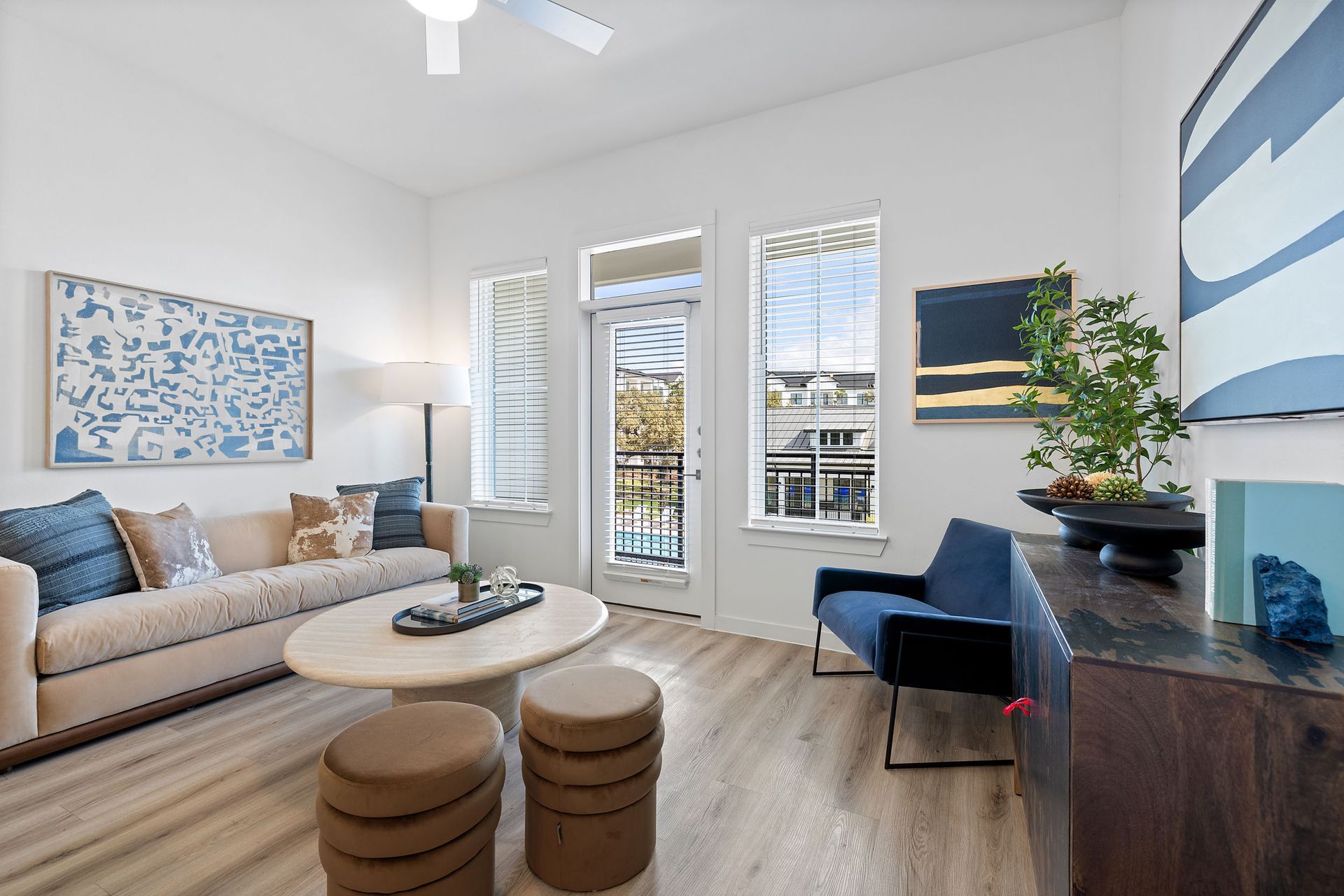 A living room with a couch, chair, coffee table, ottomans, oversized windows and exit door to balcony at The Everett, offering apartments for rent in Northwest Austin, TX.