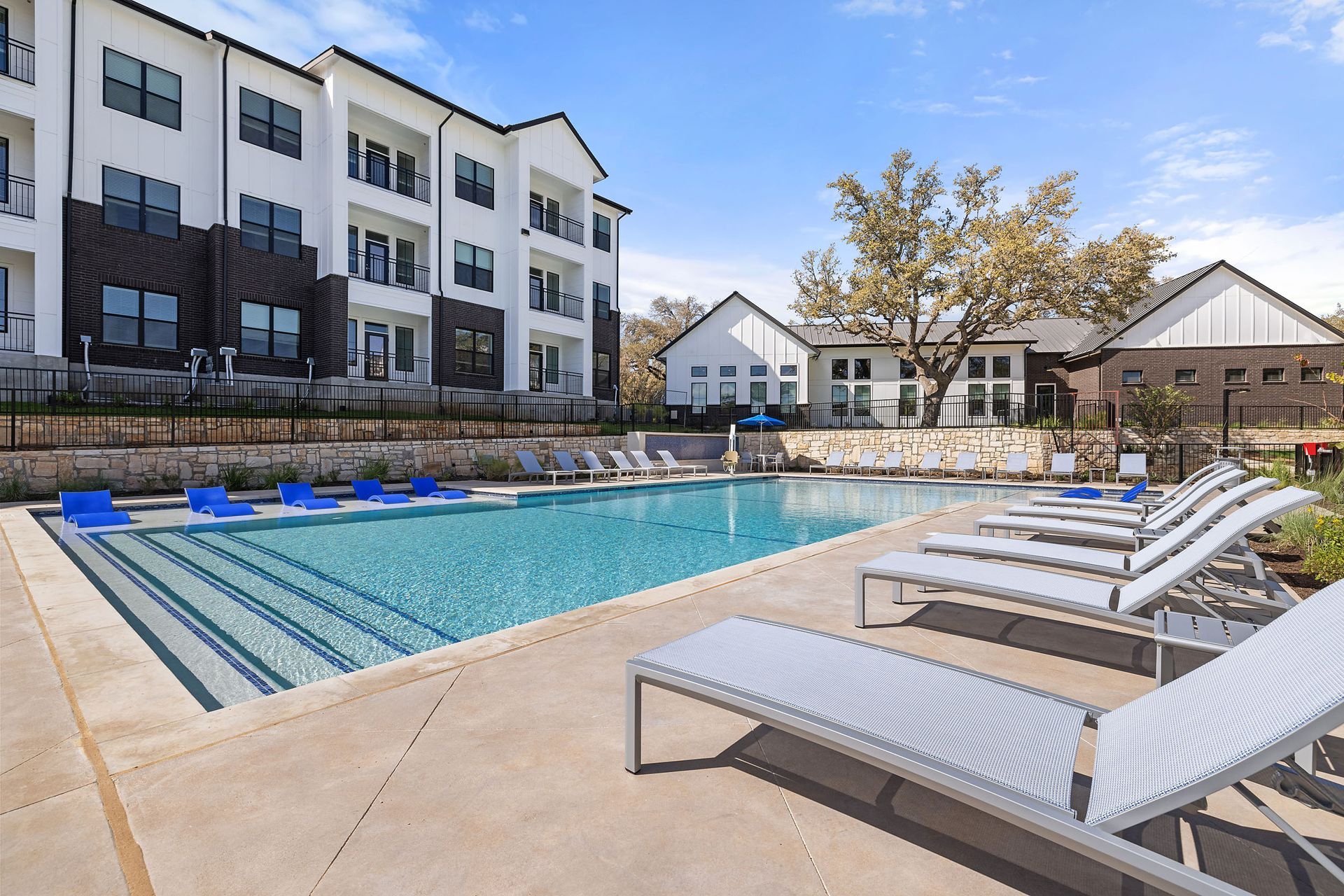Luxury apartment swimming pool surrounded by lounge chairs in front of a large apartment building at The Everett, offering apartments for rent in Northwest Austin, TX.