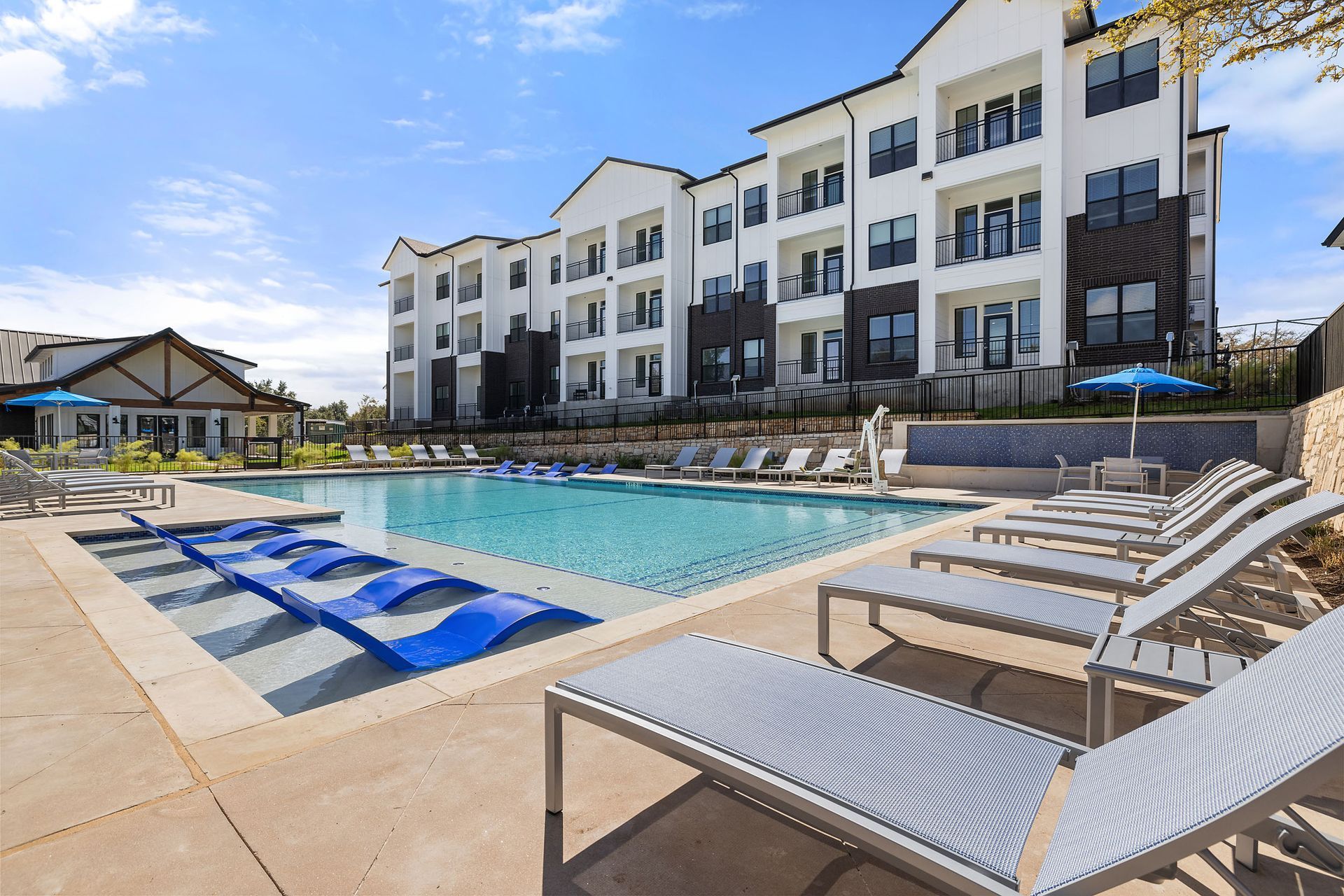A large apartment building with a swimming pool in front of it with poolside loung at The Everett, offering apartments for rent in Northwest Austin, TX.