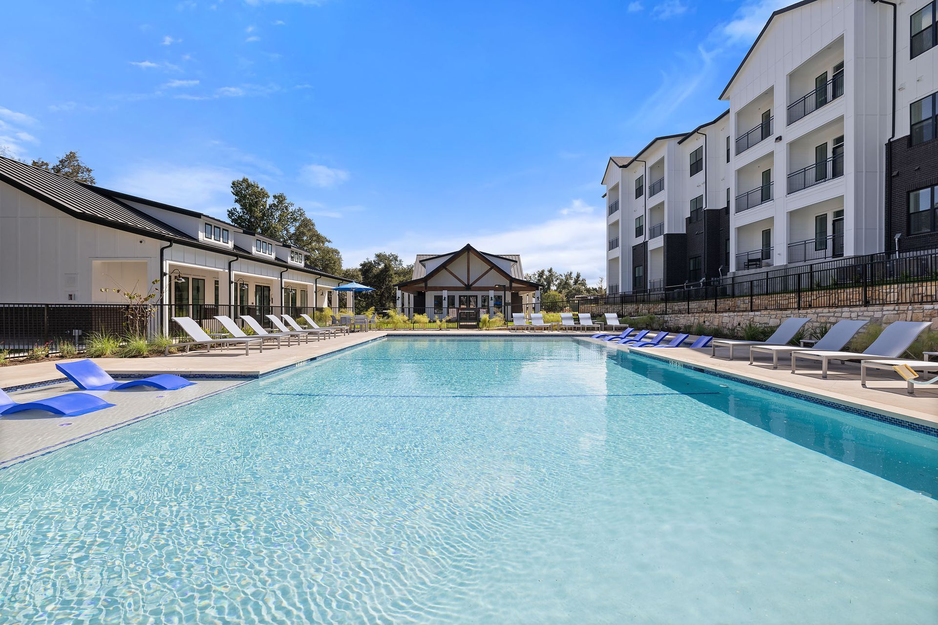Beautiful swimming pool surrounded by chairs and apartment buildings with blue sky at The Everett, offering apartments for rent in Northwest Austin, TX