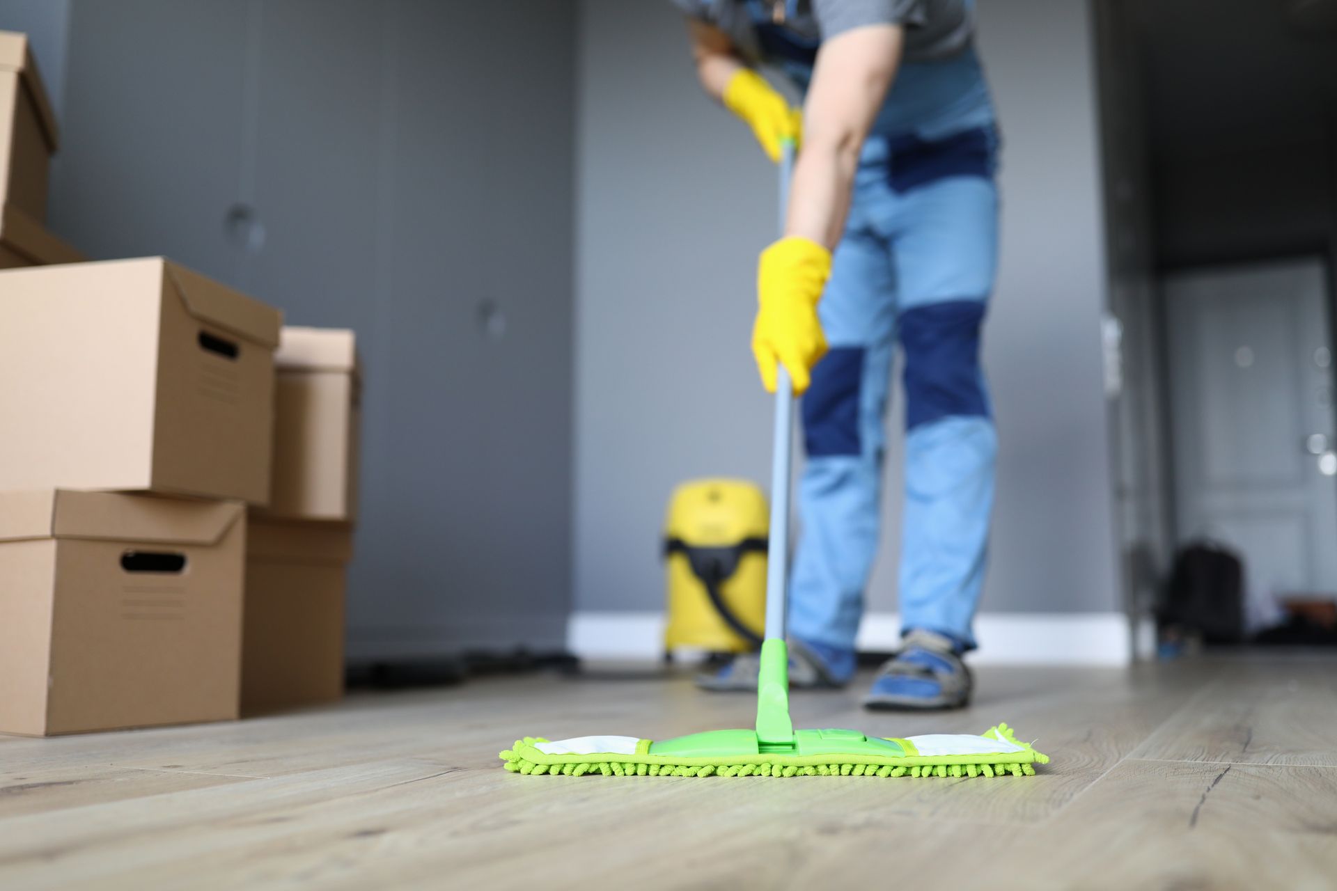 Person in gray coveralls vacuums a concrete floor with a yellow vacuum.