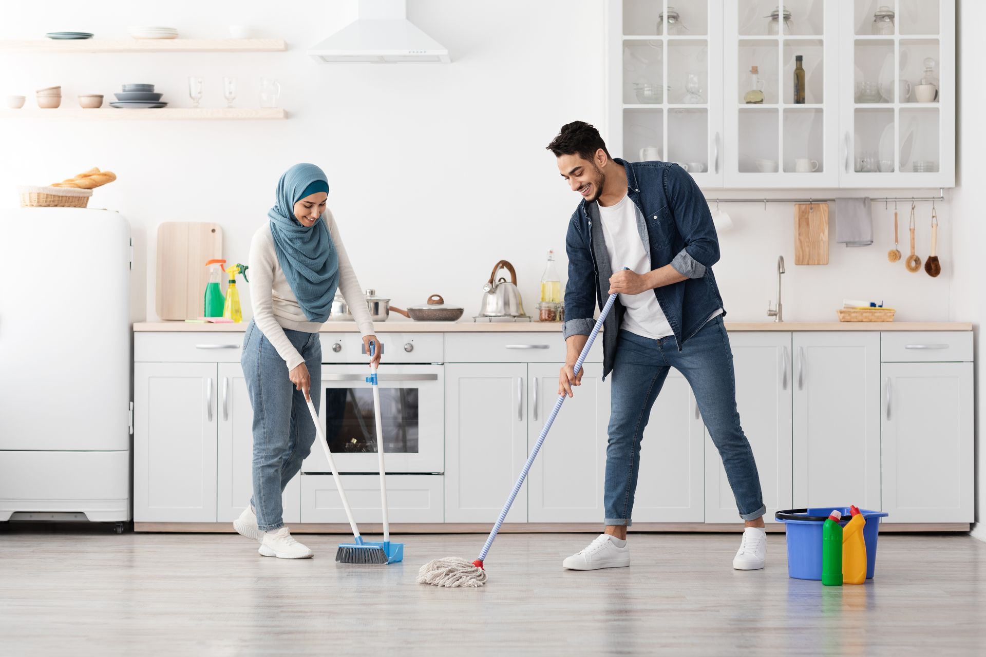 Two people shoveling rubble into black trash bags on a concrete floor.