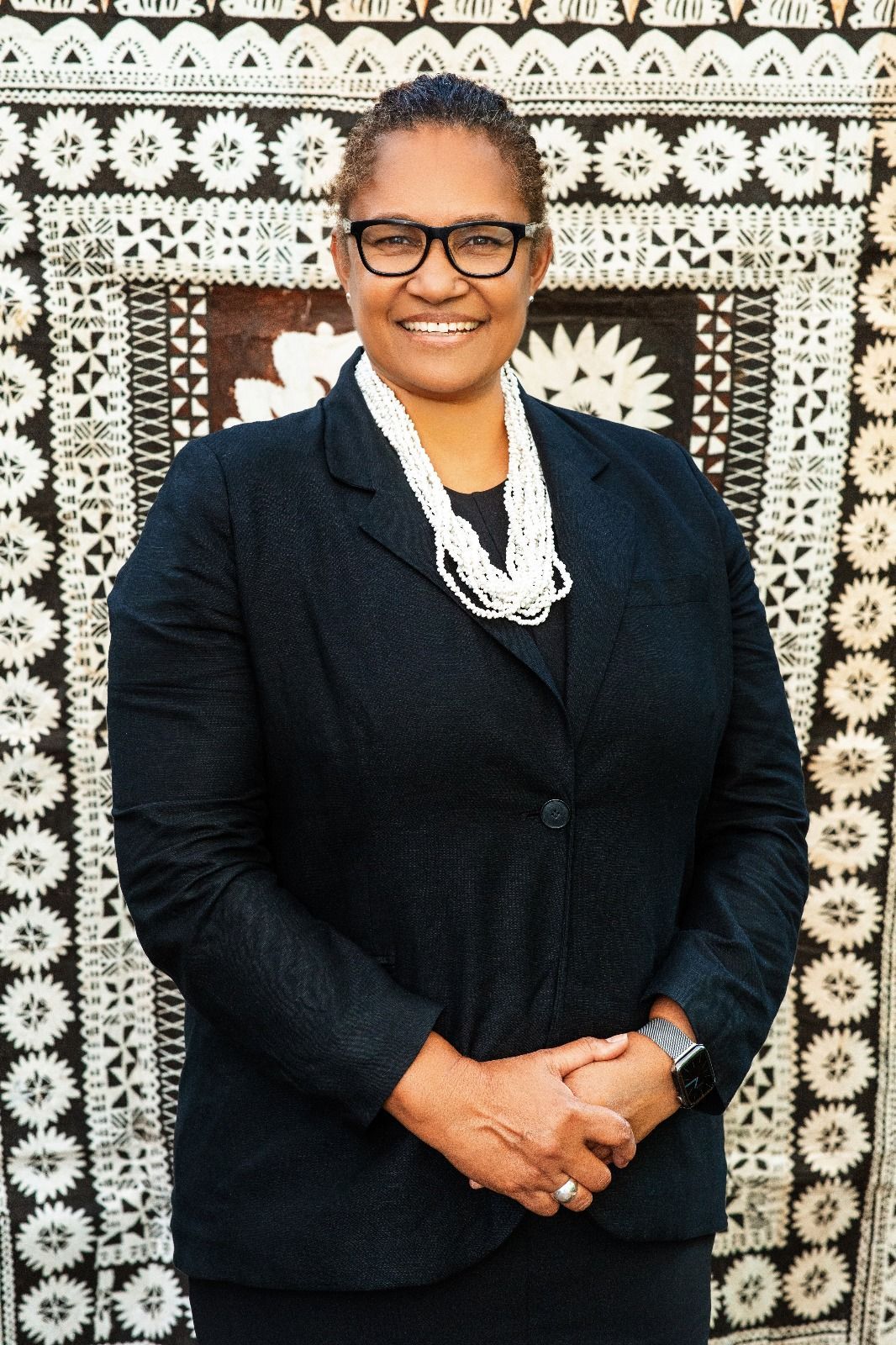 A woman wearing glasses and a black jacket is standing in front of a rug.