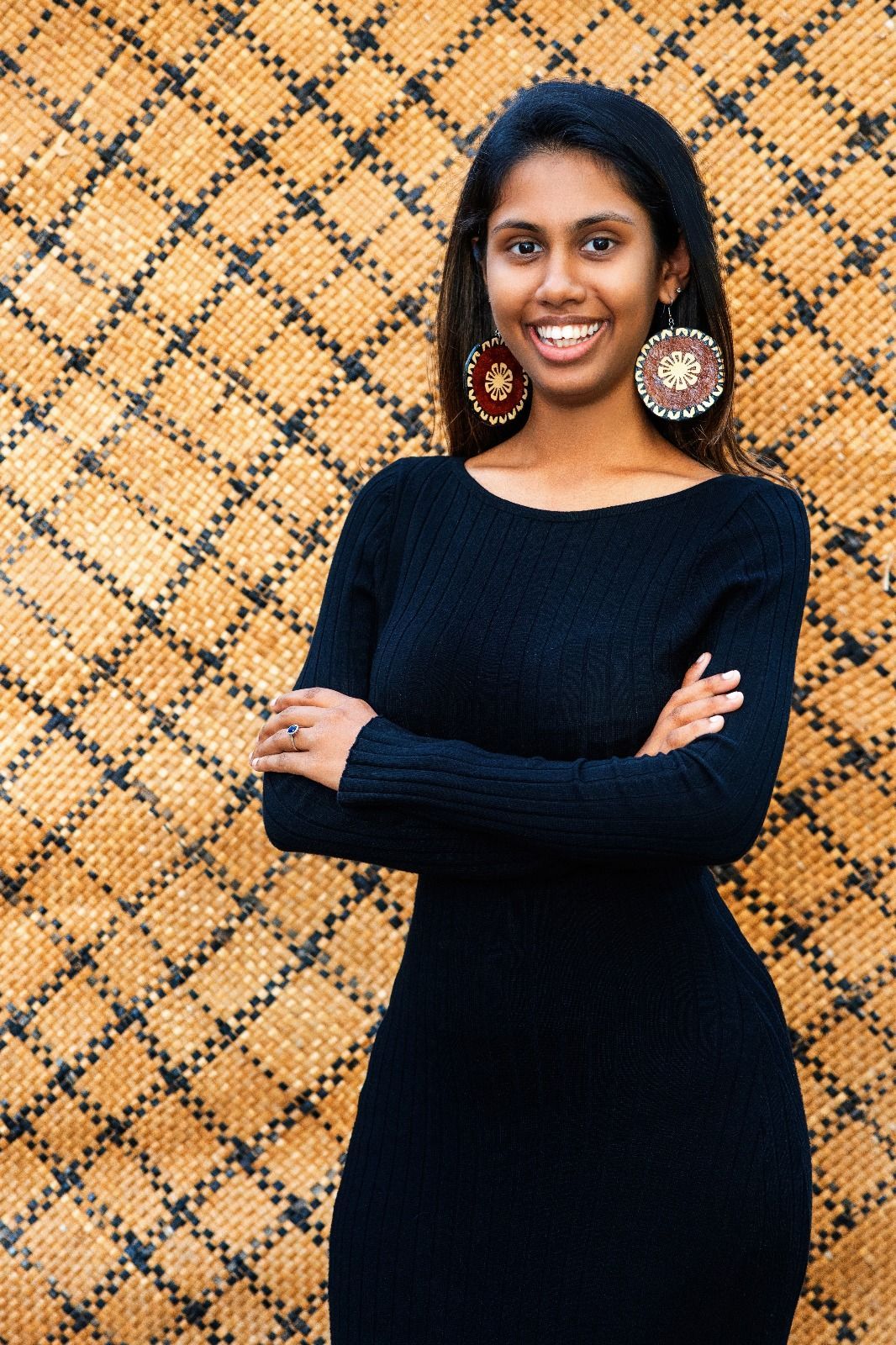 A woman in a black dress is standing with her arms crossed