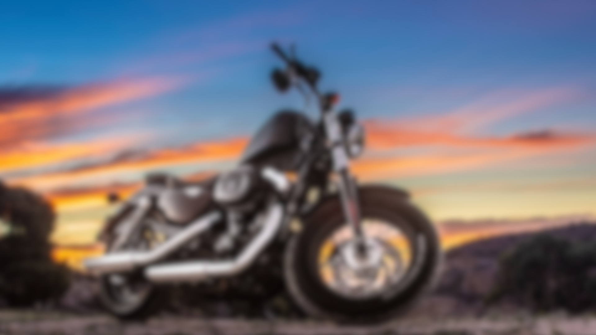 A motorcycle is parked on a dirt road at sunset.