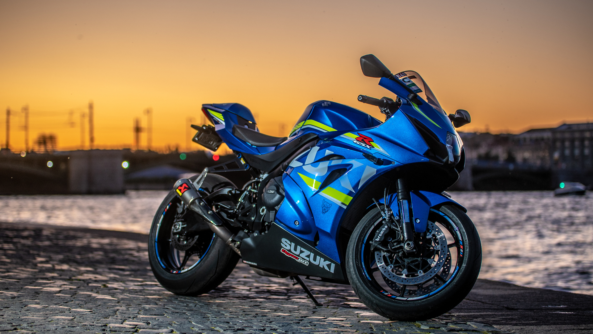 A blue motorcycle is parked next to a body of water at sunset.