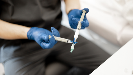 A person wearing blue gloves is holding a syringe in their hands.