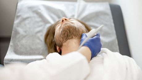 A man is laying on a bed getting a beard treatment.