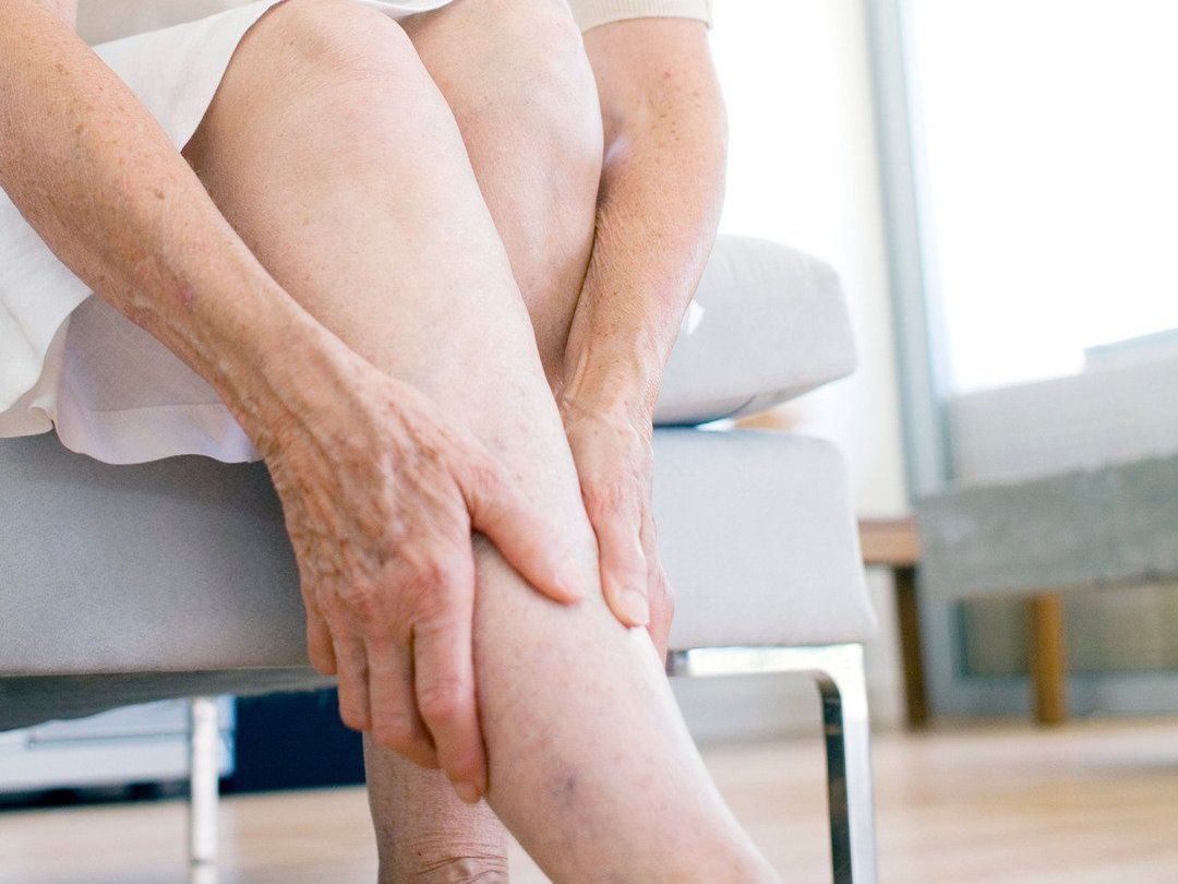 A woman is sitting on a couch holding her leg in pain.