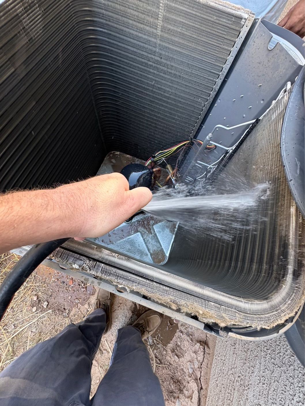 Person spraying water into an air conditioning unit's coils with a hose.