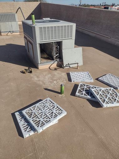 Electrician in yellow hard hat and overalls, working on electrical panel near a window.