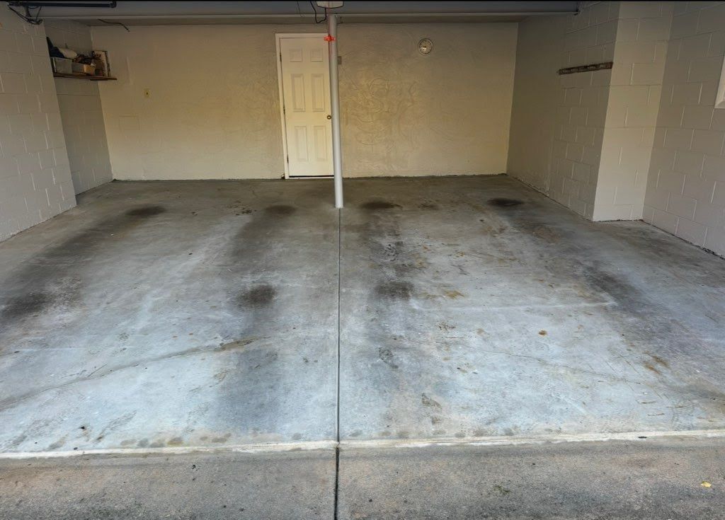 Empty garage with concrete floor, centered support pole, and a closed door. Dark stains are visible on the floor.