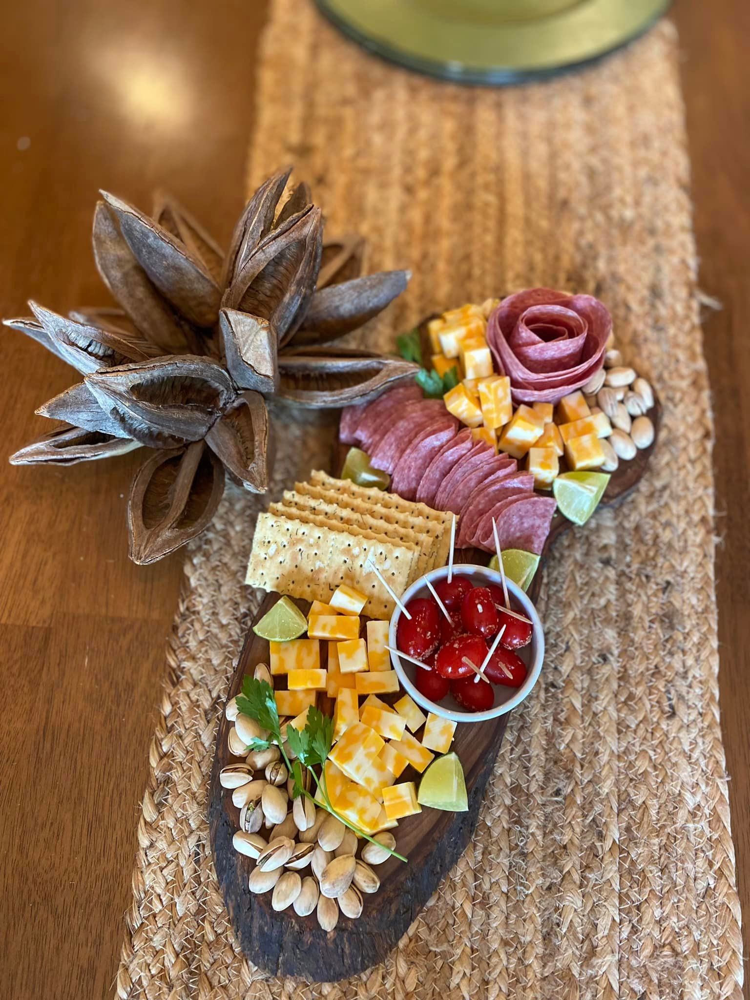 A wooden cutting board filled with meat , cheese , crackers , nuts and cherry tomatoes.