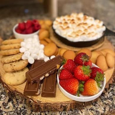 A wooden cutting board topped with strawberries , cookies , marshmallows and a cake.