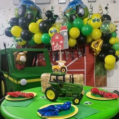 A table with plates , napkins , balloons and a toy tractor on it.