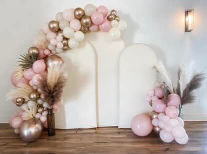 A room decorated with pink and gold balloons and pampas grass.